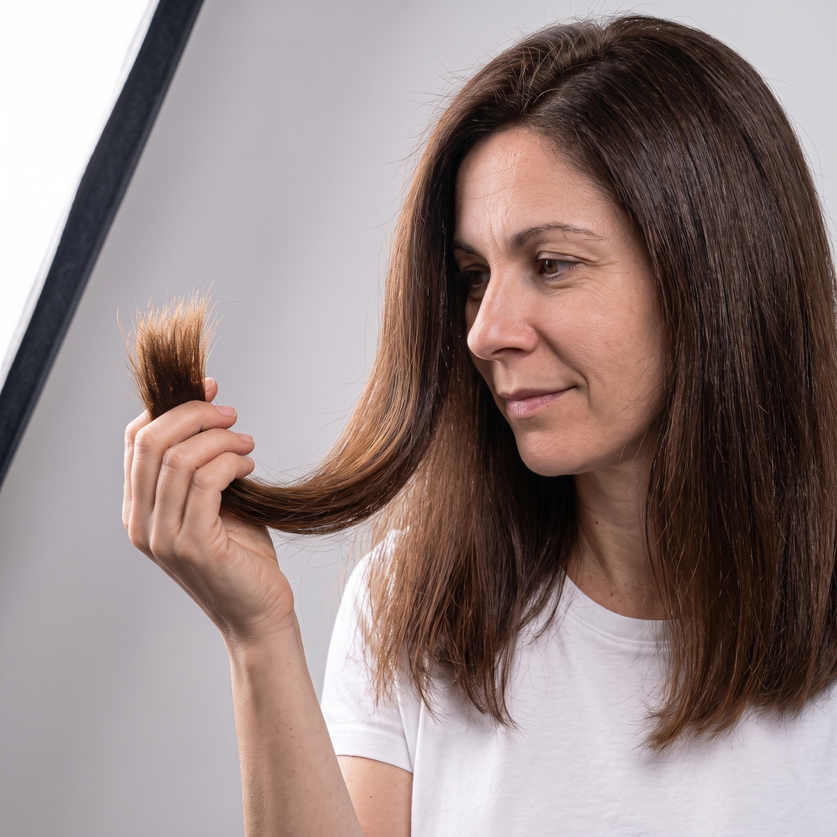 The same woman holding up a lock of smooth, glossy, well-defined hair after using the Bledna routine